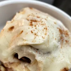 A sourdough cinnamon roll topped with thick cream cheese icing on a white plate