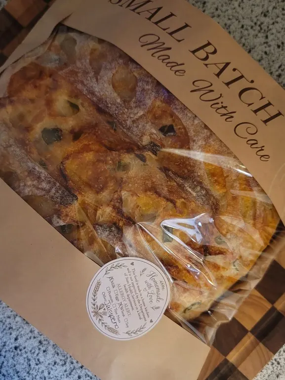 A jalapeño cheddar sourdough loaf in a kraft sleeve printed “Small Batch — Made With Care”, with a Homemade with Love label