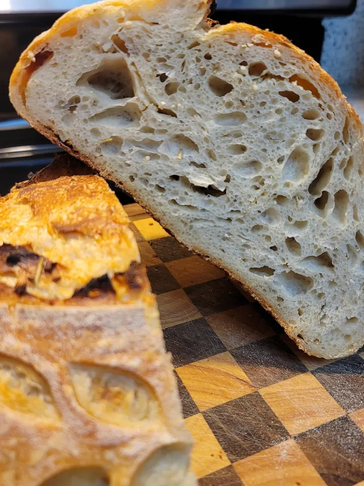 A sliced sourdough loaf showing its open, airy crumb on a checkered cutting board