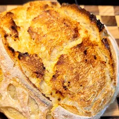 A round, deeply golden rosemary and garlic sourdough boule on a checkered cutting board