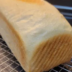 A tall, soft sourdough sandwich loaf cooling on a wire rack